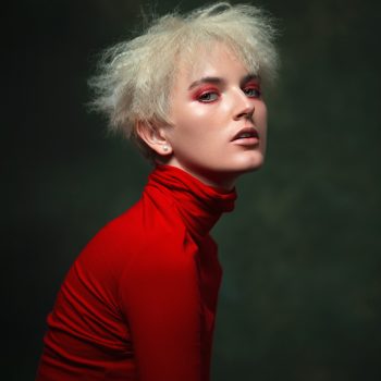 Portrait of a woman with blonde messy hair wearing a red sweater looking into the camera